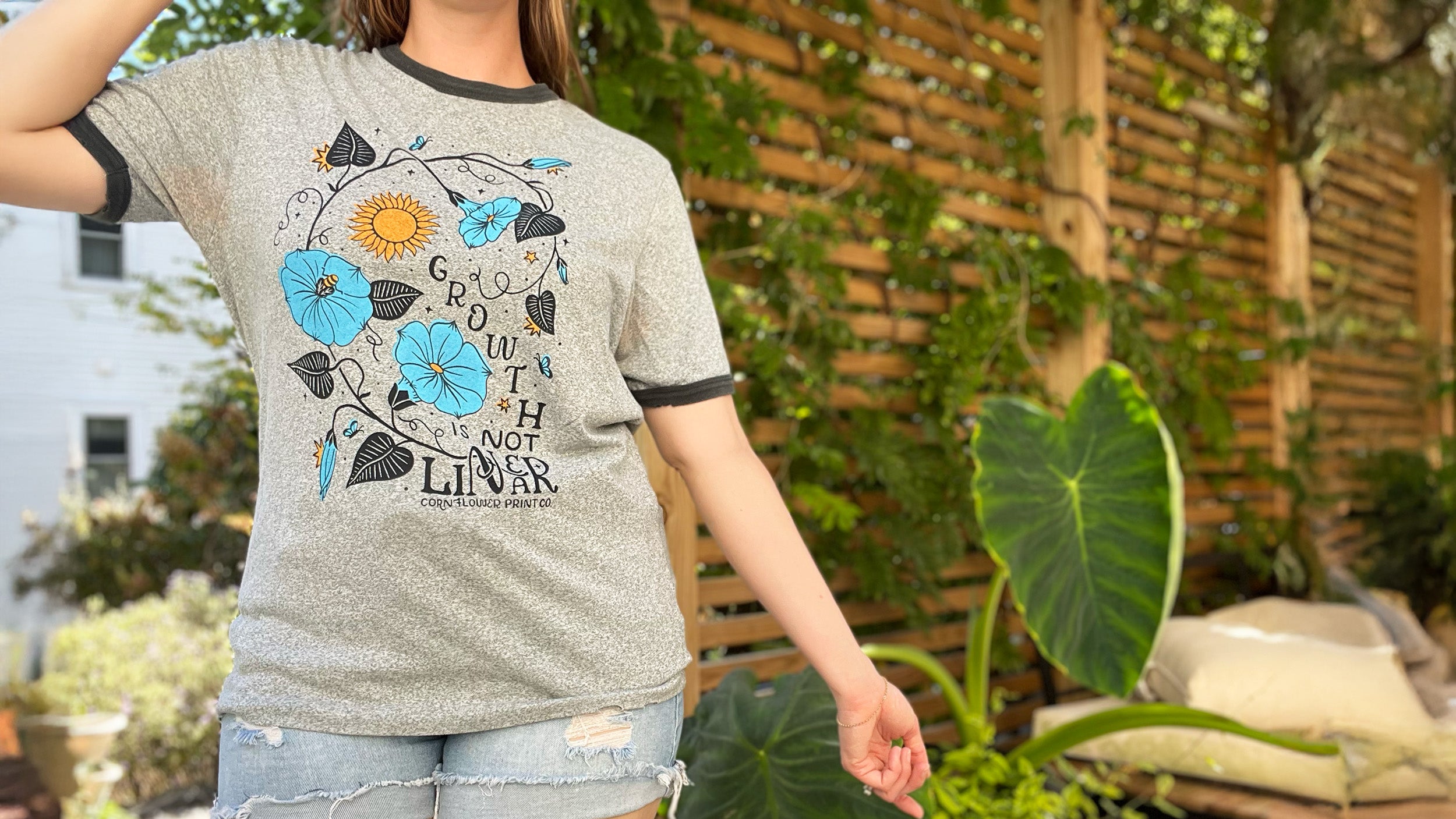 Person wearing a gray t-shirt with floral design and text in an outdoor setting