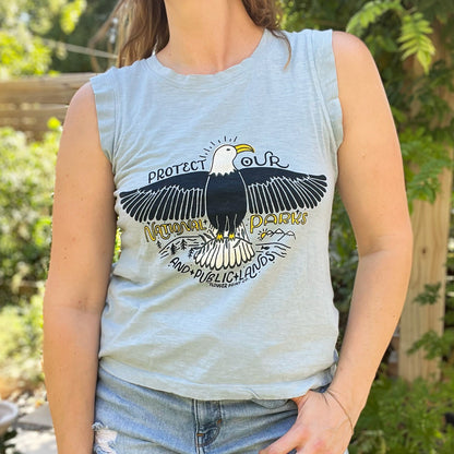 Person wearing a sleeveless light blue shirt with an eagle graphic and text about protecting national parks. Protect Our National Parks. hand-pulled screenprinted illustration on thrifted apparel, handmade, upcycled apparel