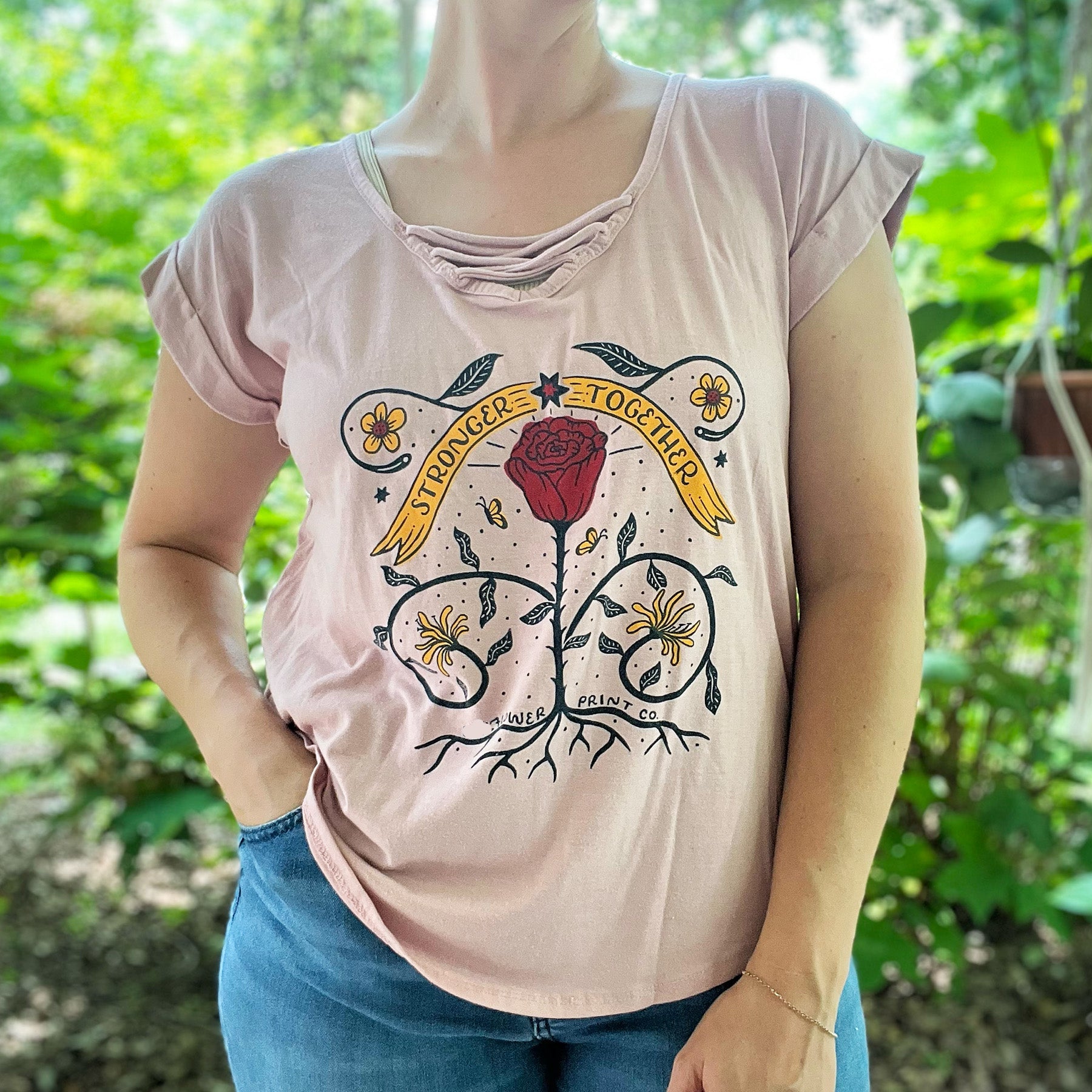 Person wearing a pink t-shirt with a floral design and text in a natural setting. June birth flowers of rose and honeysuckle. Hand-pulled screenprinted original illustration by Cornflower Print Co.