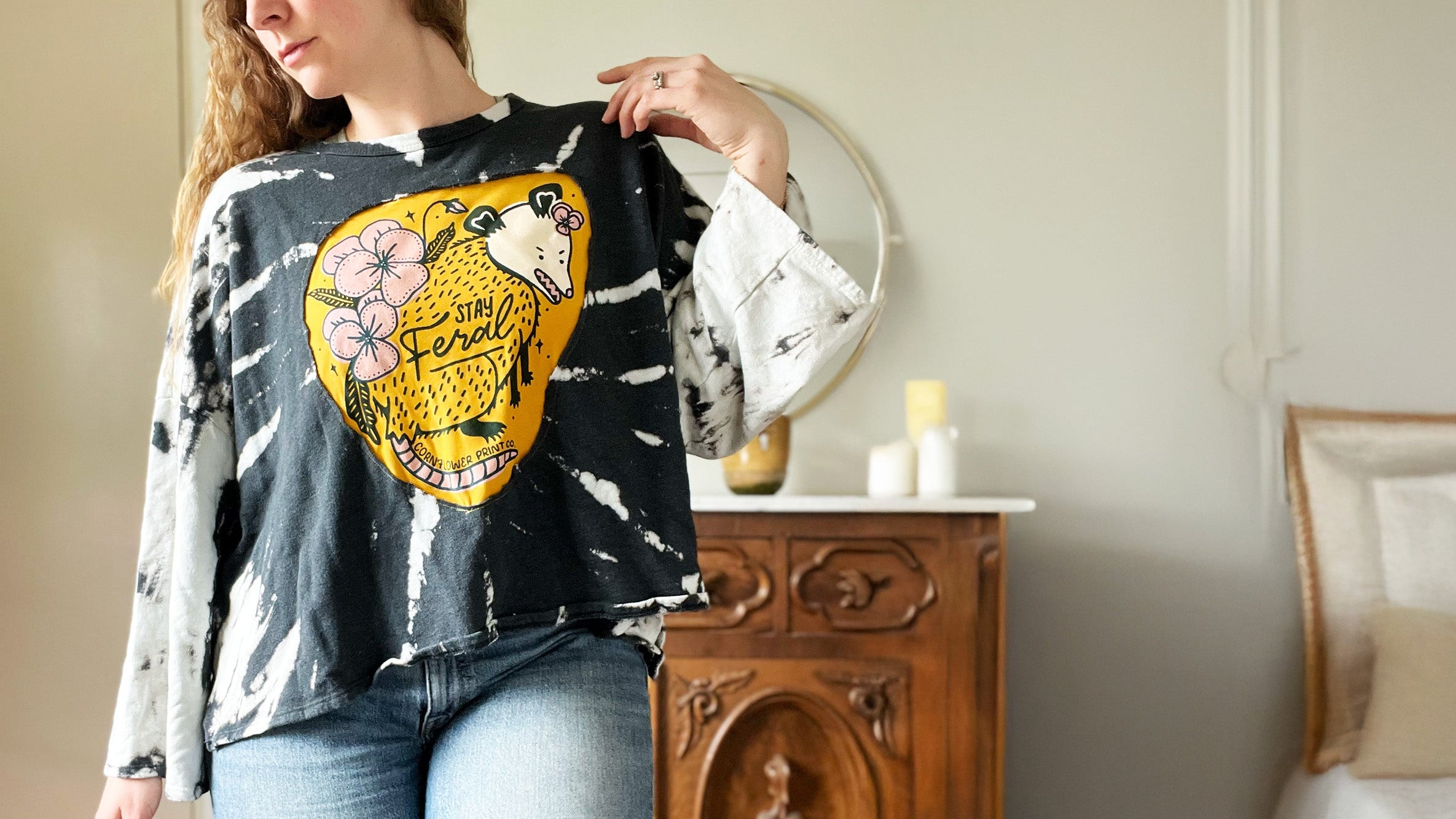 Person wearing a black tie-dye shirt with a colorful opossom design in a room.