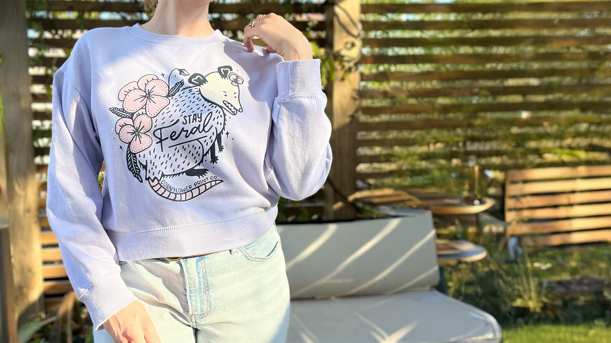 Person wearing a light blue sweatshirt with a graphic design outdoors.