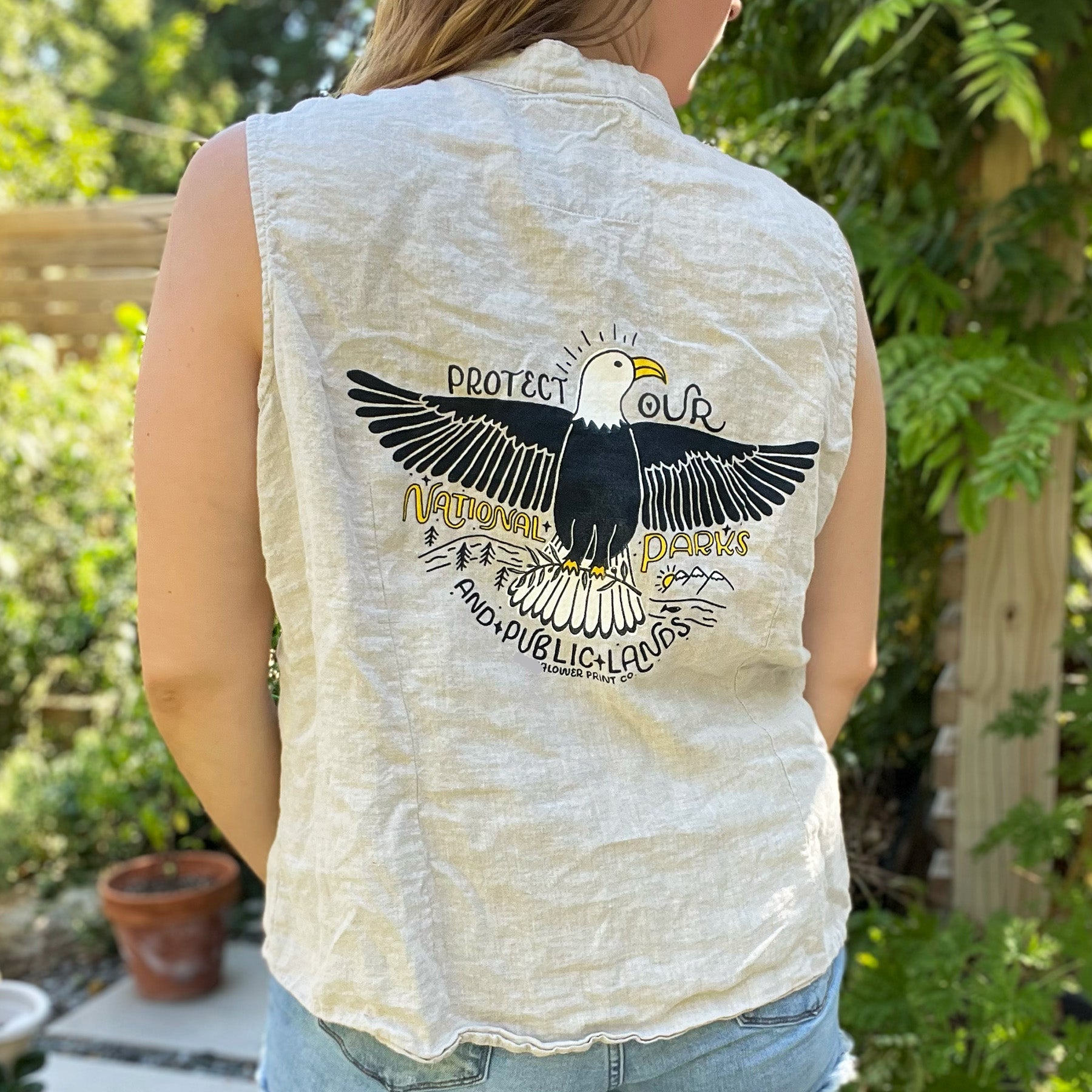 Person wearing a sleeveless shirt with an eagle design and text outdoors. Protect Our National Parks. hand-pulled screenprinted illustration on thrifted apparel, handmade, upcycled apparel