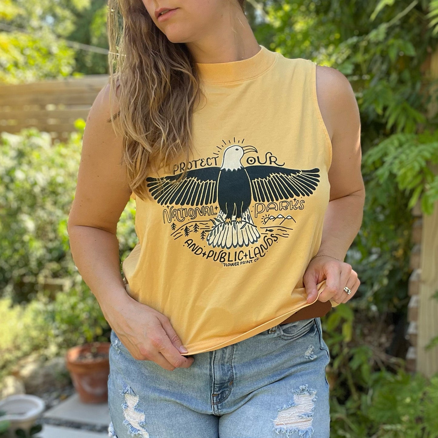 Person wearing a yellow tank top with an eagle design outdoors. Protect Our National Parks. hand-pulled screenprinted illustration on thrifted apparel, handmade, upcycled apparel